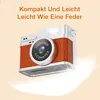 A vintage-style digital camera is shown against a light beige background with a feather graphic underneath. Produktbild-Vorschau