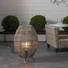 An outdoor patio setting with a woven lamp and chair. Produktbild-Vorschau