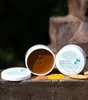Two tubs of Keralit Undercover Pflegepaste are displayed on a rustic surface, with colorful powders and a piece of ginger scattered around them. Produktbild-Vorschau