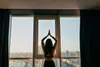 A woman is doing yoga in front of a large window with a city view. Podgląd zdjęcia produktu