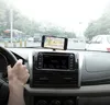 A person's hand is on the steering wheel of a car, with a smartphone mounted on the dashboard displaying a navigation app. Náhled obrázku produktu