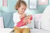 A young girl is feeding a baby doll with a bottle while sitting on a couch. Náhľad obrázku produktu