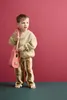 A young boy stands holding a pink toy guitar against a pink background. Produktbild-Vorschau
