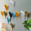 Several bird-shaped wall hooks are displayed on a light gray wall, with a lamp and plants in the foreground. Voir les images du produit