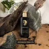 A perfume bottle is displayed amongst natural elements like wood and rocks, with a dark background. Náhled obrázku produktu