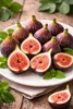 A plate of fresh figs, some whole and some halved, with mint leaves, on a wooden table. Podgląd zdjęcia produktu