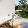 An outdoor sink area with a marble countertop, a sink with a faucet, and a garden setting with a table and chairs in the background. Produktbild-Vorschau