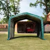 A green fabric shelter is set up on a grassy area, with a red truck and a quad bike visible inside the shelter. A wooden barn-like structure is behind the shelter. Voir les images du produit