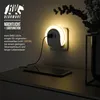 A night light with USB charging function plugged into a wall outlet, illuminating a bedside table with a smartphone charging. Produktbild-Vorschau