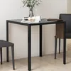 A square dining table with a glass top and black metal legs, set in a room with two chairs and a vase of flowers. Podgląd zdjęcia produktu
