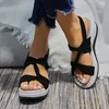 Schwarze Plateau-Sandalen mit Stoffknotenriemen an Füßen mit weißer Pediküre, getragen mit ausgefranster blauer Jeans Anteprima dell’immagine prodotto