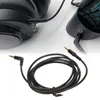 A black audio cable with 3.5mm connectors is shown coiled in the foreground, with a close-up of headphones and a speaker in the background. Náhled obrázku produktu