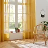 A room with yellow curtains, a wicker chair, and a window overlooking greenery. Produktbild-Vorschau
