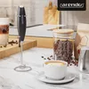 A kitchen counter with a milk frother, a cup of coffee, and coffee beans. Produktbild-Vorschau