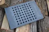 A cast iron grate with holes sits on a pile of firewood. Produktbild-Vorschau