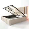 A beige upholstered bed frame with its storage mechanism open, revealing the slatted mattress support and internal storage space. The headboard has padded panels and integrated LED lighting. Voir les images du produit