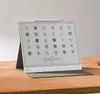 A digital e-reader with a stylus is displayed on a wooden desk, propped up by a green case. Produktbild-Vorschau