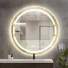 A round, gold-framed mirror with integrated LED lighting is mounted on a tiled wall above a bathroom vanity. Produktbild-Vorschau