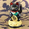 A black Maneki-neko figurine sits on a pile of gold coins against a marbled gold and dark blue background. Produktbild-Vorschau