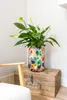 A peace lily plant in a colorful floral vase sits on top of a wooden crate. Voir les images du produit