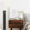 A black tower fan is placed next to a wooden nightstand with a framed picture and a vase with dried flowers. Náhled obrázku produktu