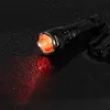 A black flashlight with a red light beam is placed on a wet, dark surface. Podgląd zdjęcia produktu