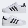 Two pairs of white Adidas Superstar sneakers with black stripes and accents, shown from the side. Produktbild-Vorschau