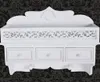 A white wall-mounted shelf with three drawers and two hooks against a dark patterned background. Náhled obrázku produktu