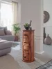 A wooden cabinet with drawers stands in a living room next to a sofa and a plant. Produktbild-Vorschau