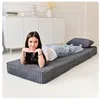 A young woman is lying on a folded mattress in a room with white furniture. Voir les images du produit