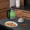 A glass electric kettle with green LED lighting is shown on a kitchen counter next to a plate of cookies and a cup of coffee. Náhled obrázku produktu