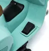 A close-up view of the footrest and part of the seat of a teal-colored children's electric scooter, resembling a Vespa. Podgląd zdjęcia produktu