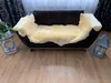 A sheepskin rug is draped over a dark brown leather sofa in a living room setting. A plant and a lantern are placed on the floor next to the sofa. Produktbild-Vorschau