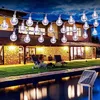 A string of solar-powered LED globe lights illuminates a backyard patio and pool area at dusk. Náhled obrázku produktu