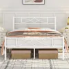 A white metal bed frame with a decorative headboard and footboard, dressed with bedding and blankets. Two storage baskets are placed underneath the bed. Produktbild-Vorschau