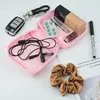 Offene rosa Reißverschlusstasche gefüllt mit Ansteckmikrofon, grünen Pillen, Foundation, Nagelknipser und USB-Stick, neben Autoschlüssel, Stift und braunem Haargummi Náhľad obrázku produktu