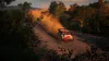 A rally car kicking up dust on a dirt road surrounded by trees. Podgląd zdjęcia produktu