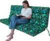 A woman is sitting on a large, green, leaf-patterned cushion, reading a book. Voir les images du produit