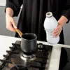 A person is holding a white plastic bottle over a black pot on a gas stove. Náhled obrázku produktu
