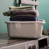 A stack of folded towels in different colors sits on top of a gray plastic basin, which is placed on a washing machine. Anteprima dell’immagine prodotto