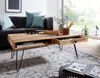 A living room scene with a coffee table in the foreground, a sofa and pillows in the background, and a window with greenery visible. Produktbild-Vorschau