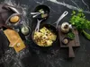 A cooking scene with ravioli in a pan, ingredients, and kitchen utensils on a dark marble countertop. Náhľad obrázku produktu