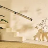 A modern interior scene featuring a minimalist staircase with a black handrail, a plant, and decorative branches in a vase on a wooden stool. Anteprima dell’immagine prodotto