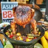 A roasted chicken is presented on a stand in a cast iron pan filled with vegetables, outdoors. Anteprima dell’immagine prodotto