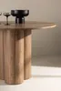 A close-up shot of a round wooden dining table with a black decorative bowl and two glasses on it. Produktbild-Vorschau