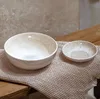 Two ceramic bowls of different sizes are placed on a textured cloth on a wooden surface. Produktbild-Vorschau