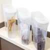 Three clear plastic food storage containers with white lids are lined up on a countertop. The leftmost container holds spaghetti, the middle one holds small grains, and the rightmost one holds chocolate cereal. Náhľad obrázku produktu