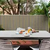 Grauer Gartentisch mit zwei Stühlen, gedeckt mit Tassen und Gebäck auf einer Terrasse mit Lamellenzaun und Bäumen im Hintergrund Produktbild-Vorschau