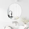 A round mirror is mounted on a white tiled wall above a sink. A faucet is visible in the mirror's reflection, along with some toiletries on a tray. A vase with dried flowers is placed next to the sink. Náhľad obrázku produktu