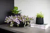 A black planter with purple flowers and a smaller black planter with green plants sit on a countertop next to two books. Produktbild-Vorschau